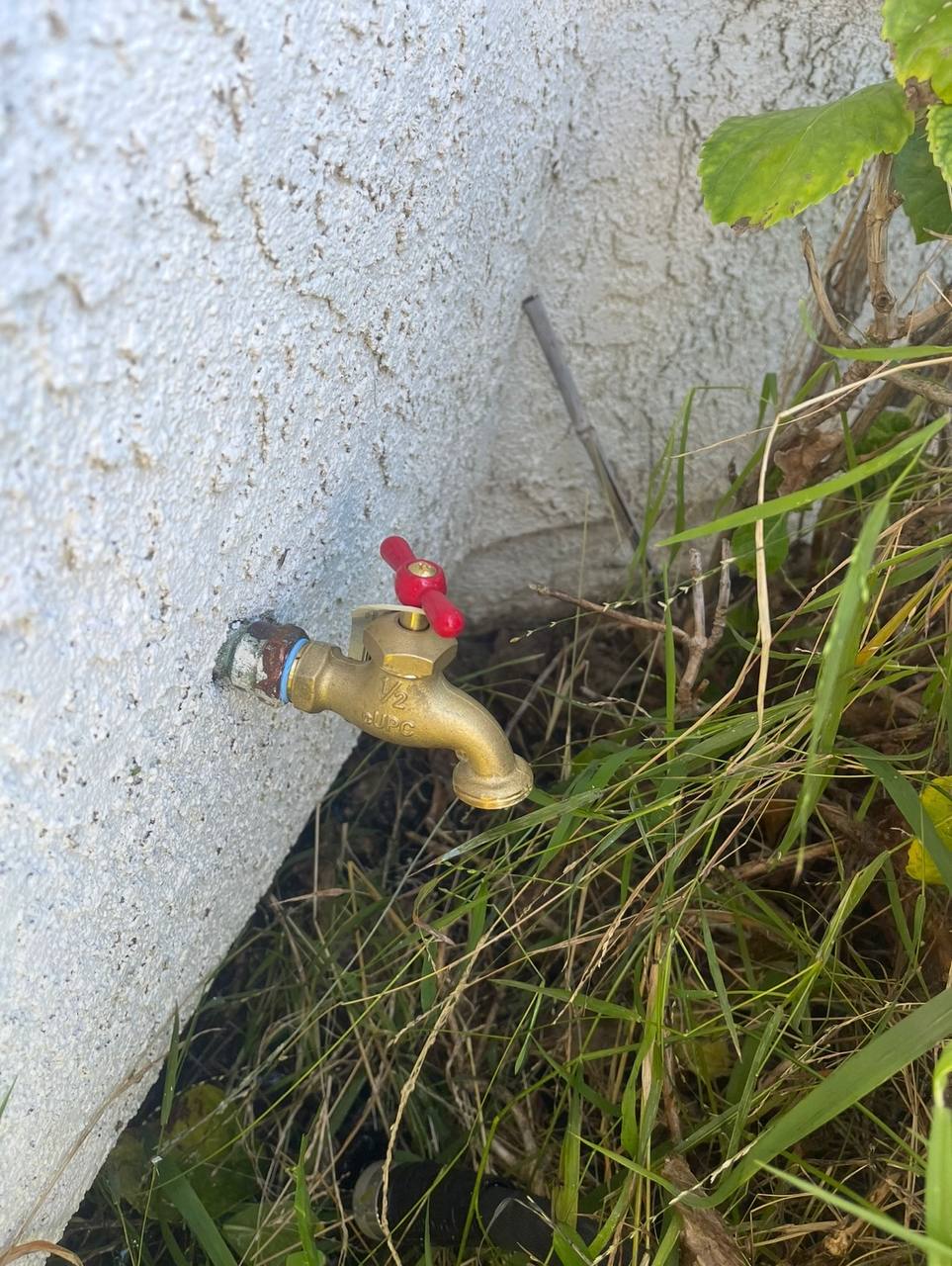 Brass outdoor water faucet with a red handle beside an exterior wall